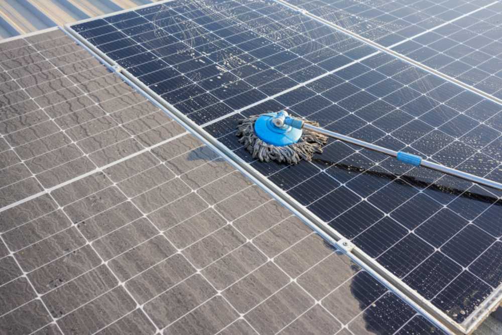A man cleaning solar panels on a roof, as part of routine solar panel maintenance in New England