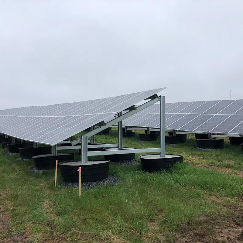 Ground-mounted solar panels installed on a grassy landfill under an overcast sky in Falmouth, MA